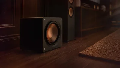A Klipsch Reference Premiere Compact subwoofer beside a floor-standing speaker